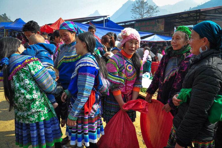 Vrouwen in Flower H'mong kleding staan in de zon te praten op de markt van Can Cau, Lao Cai.