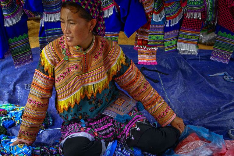 Verkoopster zit tussen geborduurde jasjes en rokken op de markt van Coc Ly, provincie Lao Cai.