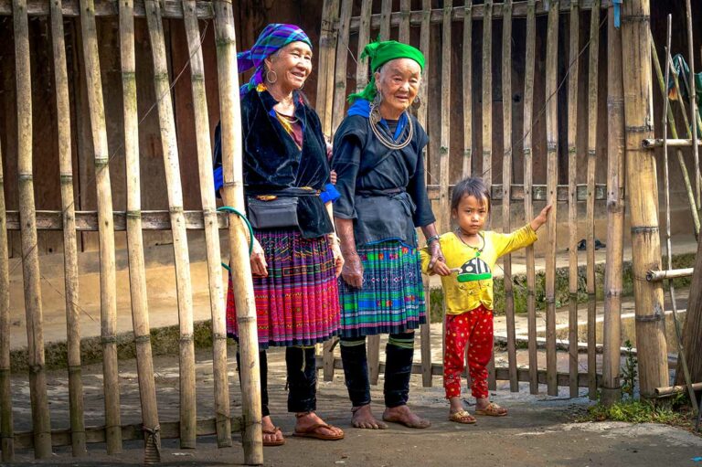 Twee oudere vrouwen in traditionele kleding met een kind bij een bamboehek in Mu Cang Chai