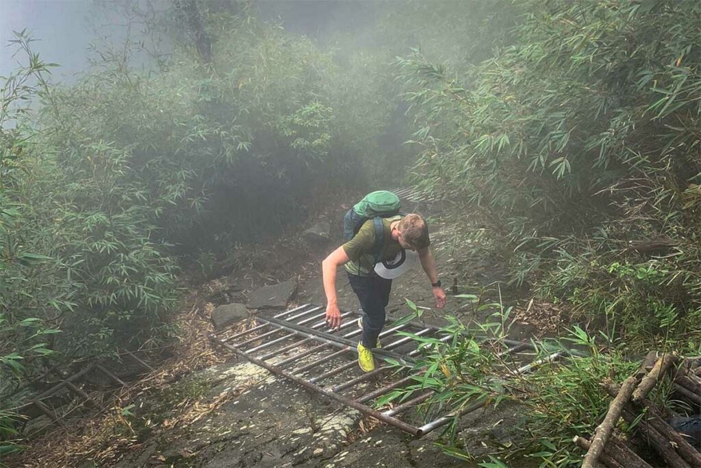 Wandelaar klimt over een metalen trap op een steil stuk van het Fansipan pad in de mist.