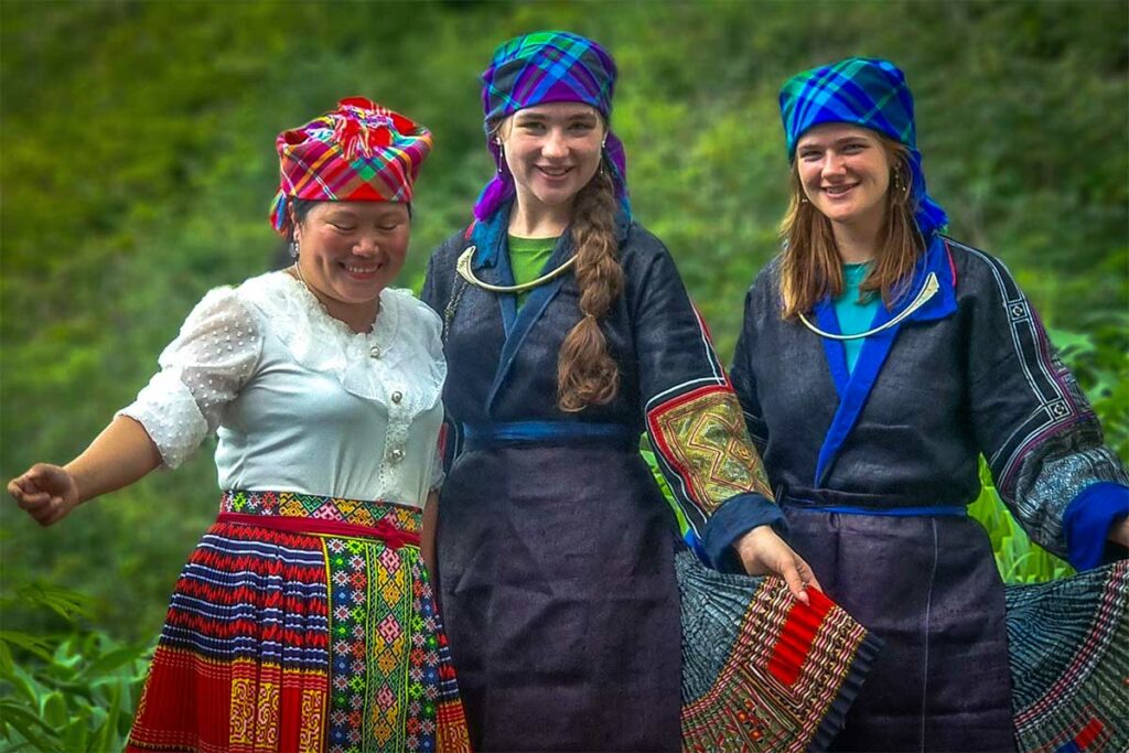Twee reizigers in geleende traditionele kleding met een lokale vrouw buiten bij een homestay in Mu Cang Chai