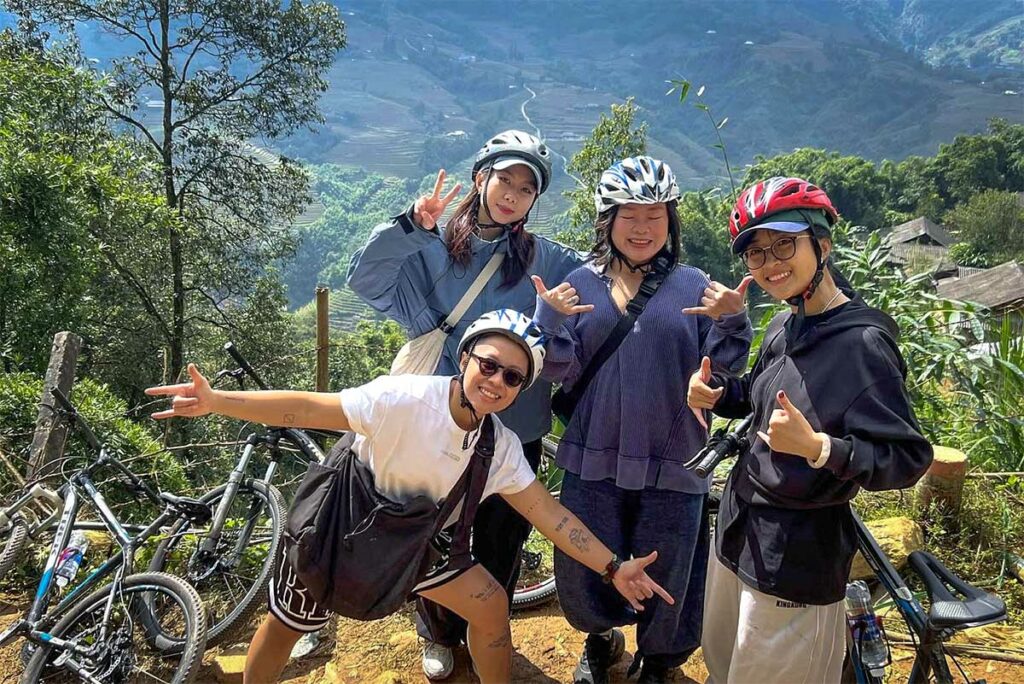 Vier fietsers met helmen poseren bij hun mountainbikes, met rijstterrassen op de achtergrond.