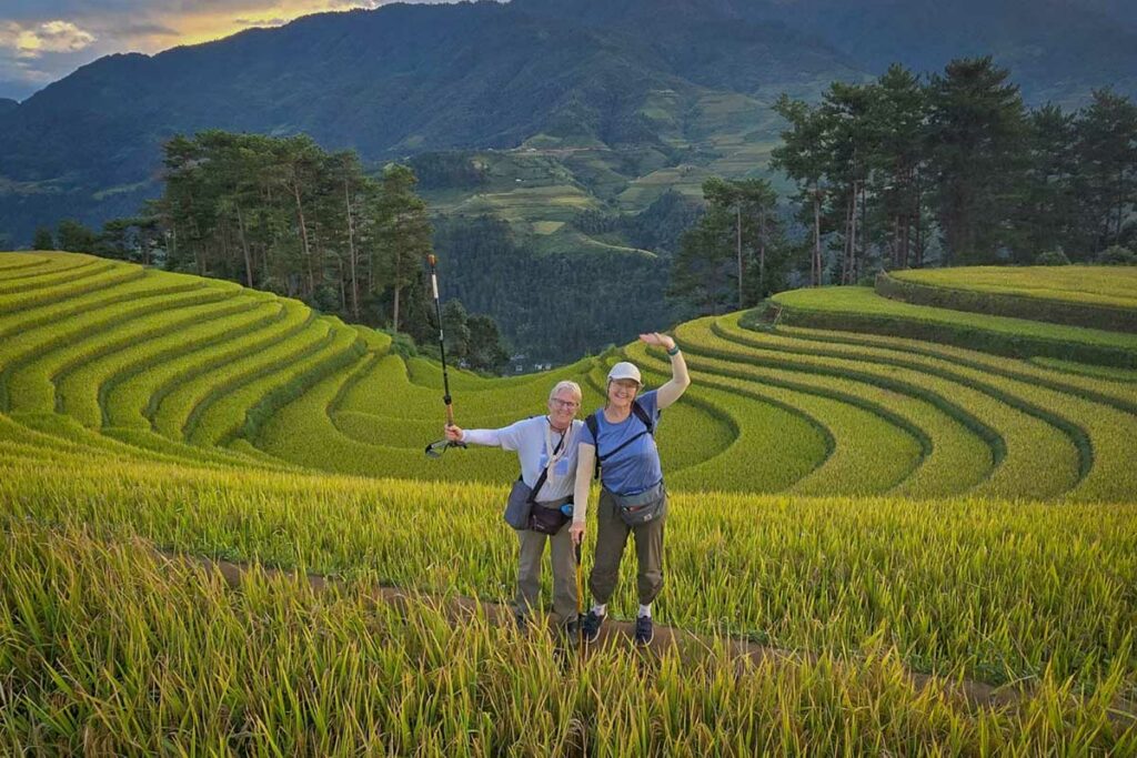 Twee wandelaars poseren tussen de gebogen rijstterrassen van Mu Cang Chai in het late middaglicht