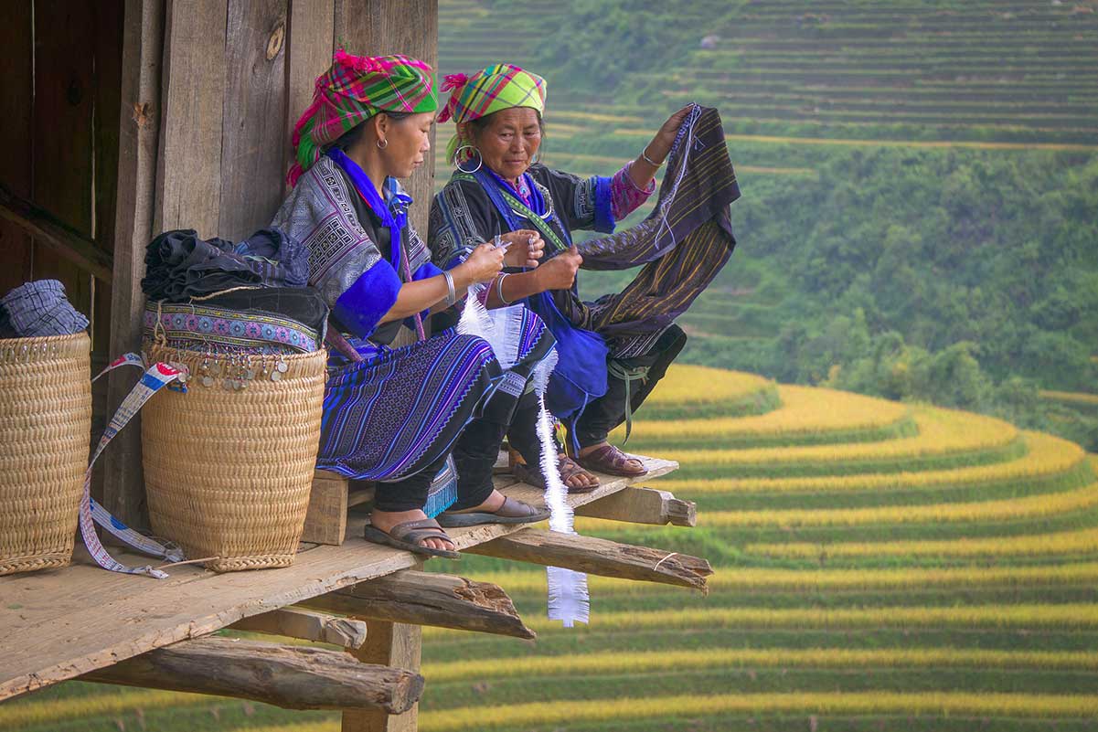 Twee vrouwen naaien op een houten platform met uitzicht over de rijstterrassen van Mu Cang Chai
