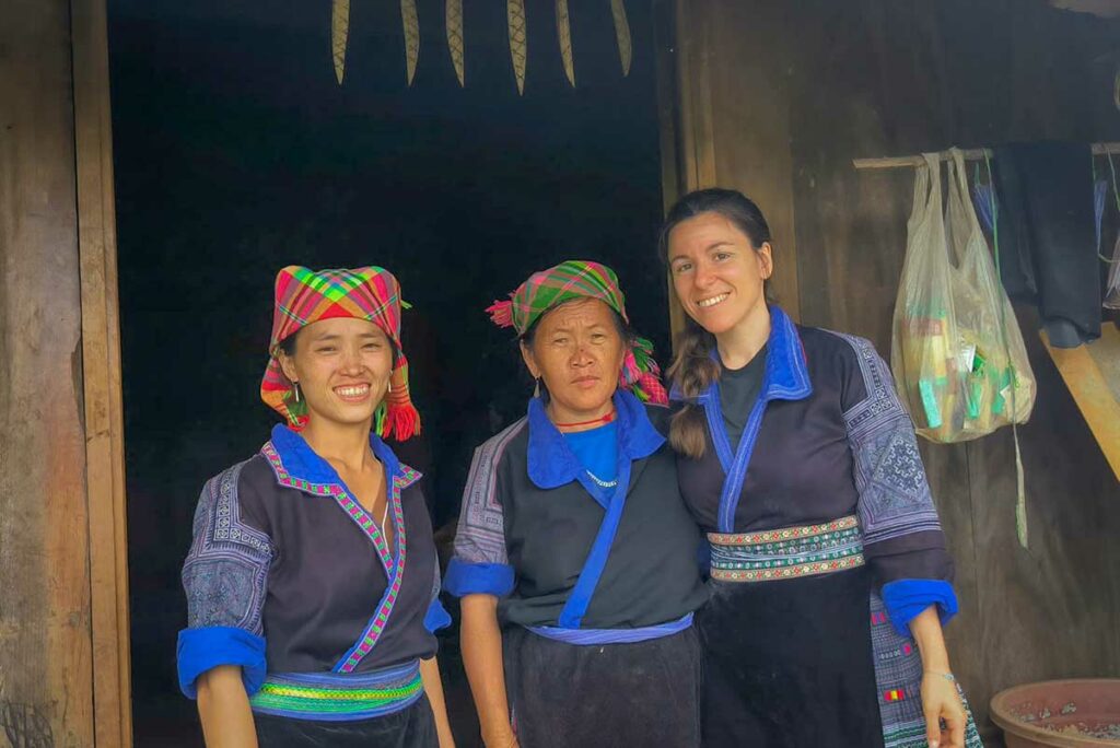 Twee lokale vrouwen en een reiziger in traditionele kleding voor een houten woning in Mu Cang Chai, Yen Bai