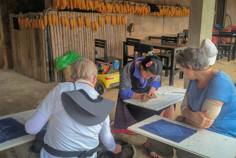 Reizigers volgen een batikworkshop onder een afdak met drogende maiskolven in Mu Cang Chai, Yen Bai