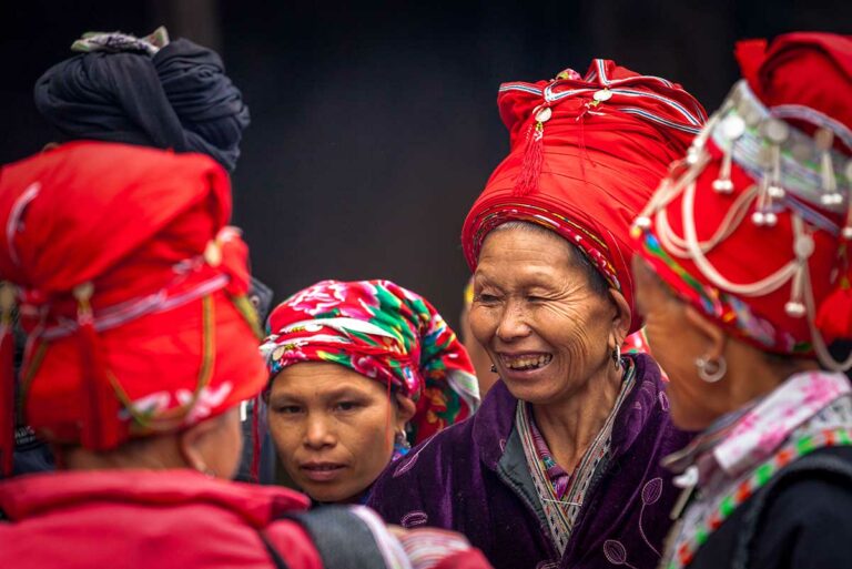 Vrouwen met rode hoofddoeken staan te praten op de markt van Muong Hum, provincie Lao Cai.