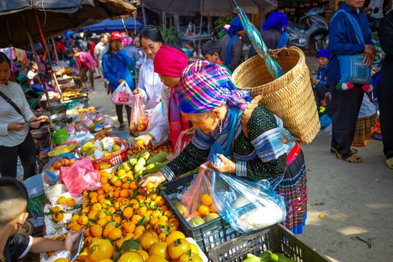 Vrouw met rugmand koopt mandarijnen bij een fruitkraam op de markt van Muong Hum.