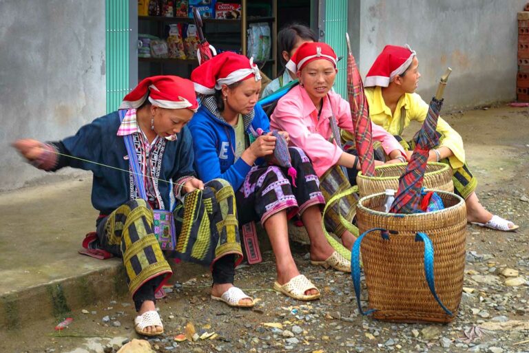 Rode Dao vrouwen met rode hoofddoeken borduren zittend voor een winkeltje in Y Linh Ho, Sapa.