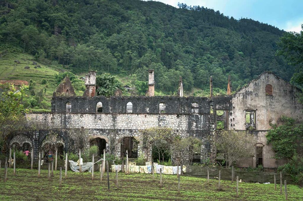Ruine van het Franse klooster bij Ta Phin, met moestuin ervoor en beboste berghelling erachter.