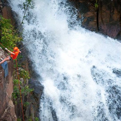 Canyoning deelnemer abseilt langs een waterval in Dalat met snelstromend water en natte rotswanden in een natuurlijke jungleomgeving