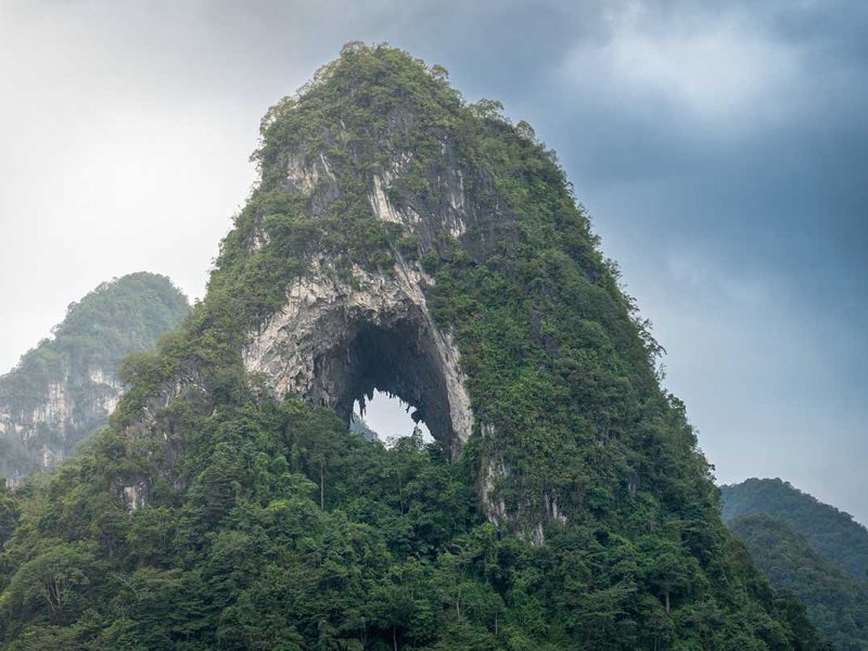 Close-up van de kalkstenen bergwand van Angel Eye Mountain met het opvallende ronde gat, begroeid met dichte vegetatie.