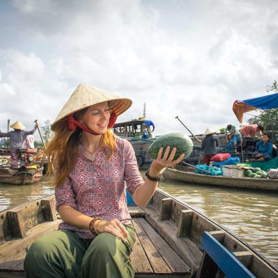 Reiziger bezoekt de drijvende markt van Cai Rang in de Mekong Delta, zittend in een houten boot tussen handelaren die fruit en groenten verkopen vanaf hun boten