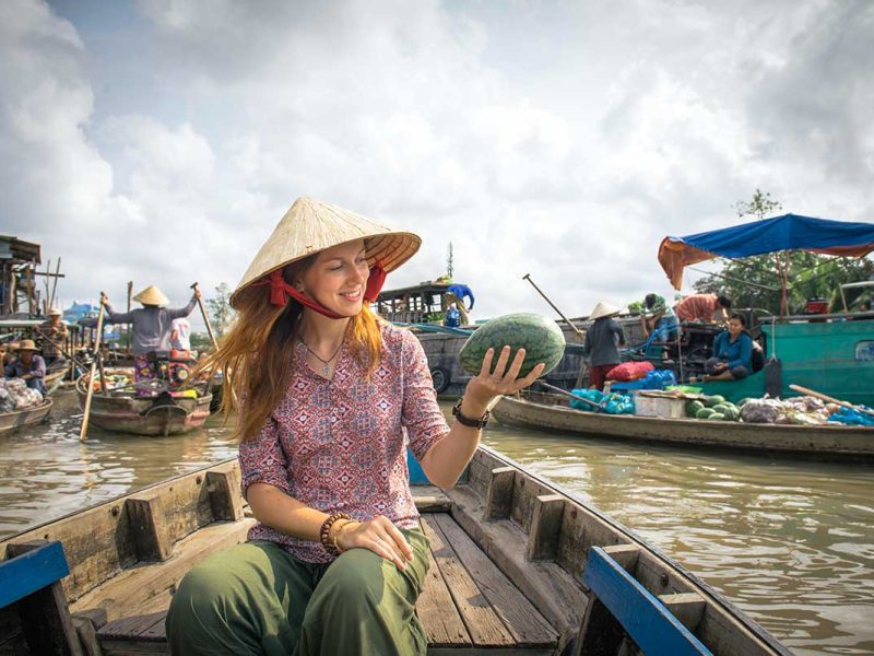 Reiziger bezoekt de drijvende markt van Cai Rang in de Mekong Delta, zittend in een houten boot tussen handelaren die fruit en groenten verkopen vanaf hun boten