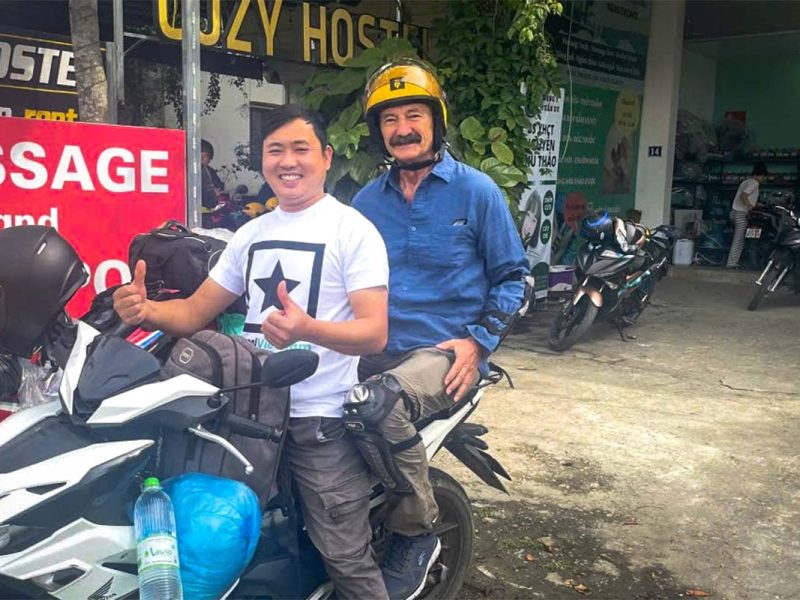 Een reiziger zit achterop bij een Local Vietnam-gids tijdens de Ha Giang Loop Easy Rider tour, klaar om te vertrekken vanuit een hostel met motoren en touruitrusting.