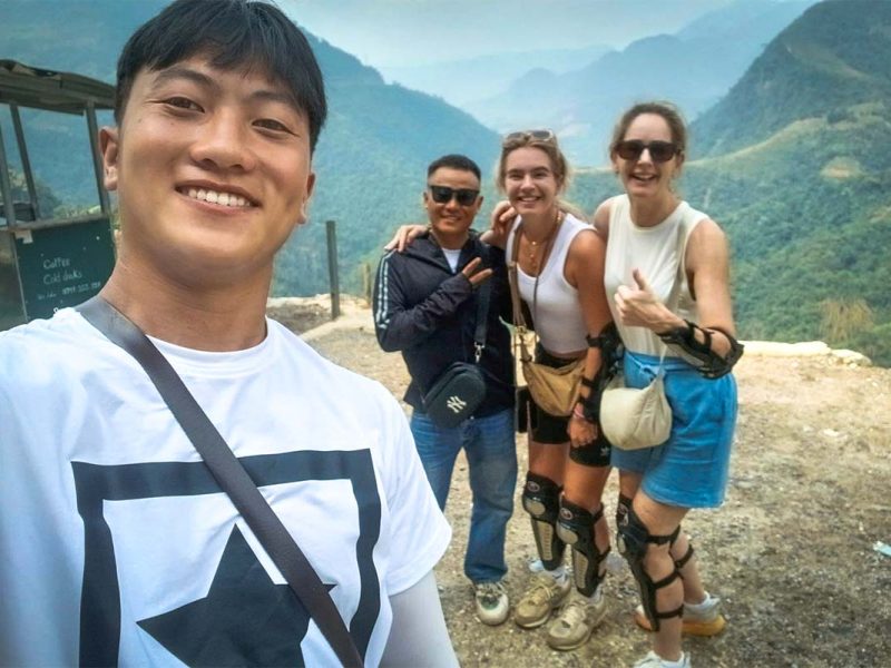 Een Local Vietnam-gids maakt een selfie met reizigers tijdens hun Ha Giang Loop Easy Rider tour, met een uitgestrekt berglandschap en diepe valleien achter hen.