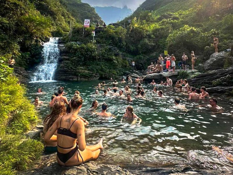 Reizigers zwemmen en ontspannen bij de Du Gia-waterval tijdens de Ha Giang Loop groepstour, omringd door rotsen, groen en stromend helder water.