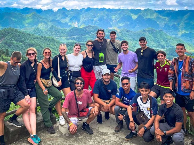 Groep reizigers die poseert op een uitzichtpunt tijdens de Ha Giang Loop, met groene karstbergen op de achtergrond.