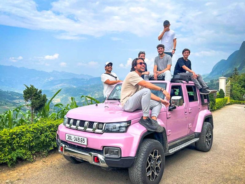 Groep reizigers op een roze jeep tijdens een Ha Giang Loop jeep tour met uitzicht over groene valleien en bergen.