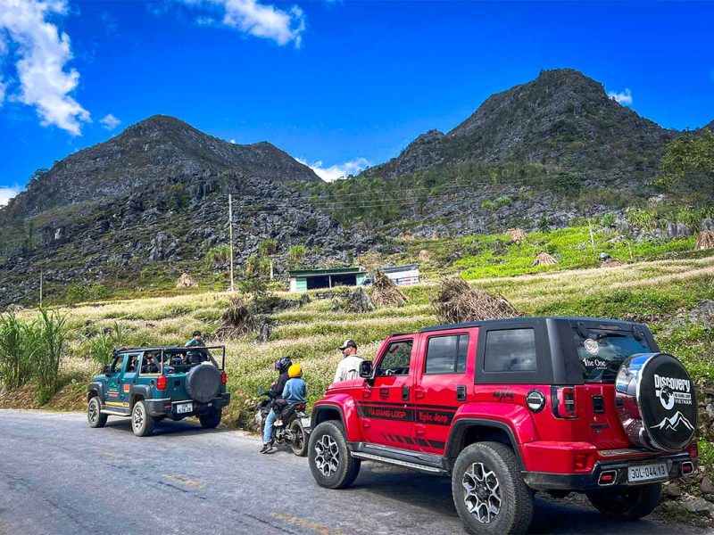 Groep reizigers met jeeps en motoren langs de Ha Giang Loop, met karstbergen en boekweitvelden op de achtergrond.