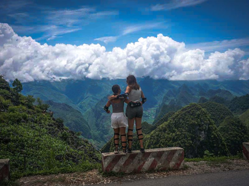 Twee reizigers op de Ha Giang Loop met Easy Rider die uitkijken over de bergtoppen bij het iconische Ma Pi Leng-uitzichtpunt.