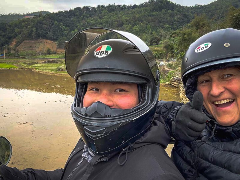 Easy Rider-gids met reiziger tijdens de Ha Giang Loop, poserend met helmen midden in een berglandschap.