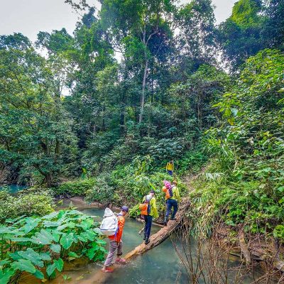 Trekkinggroep steekt een ondiepe rivier over in de jungle van Hang Ma Valley bij Phong Nha, omringd door dicht groen en ruig terrein