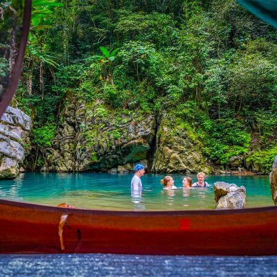 Reizigers zwemmen in een natuurlijke poel bij het kamp in Hang Ma Valley met tenten op de oever en jungle rondom