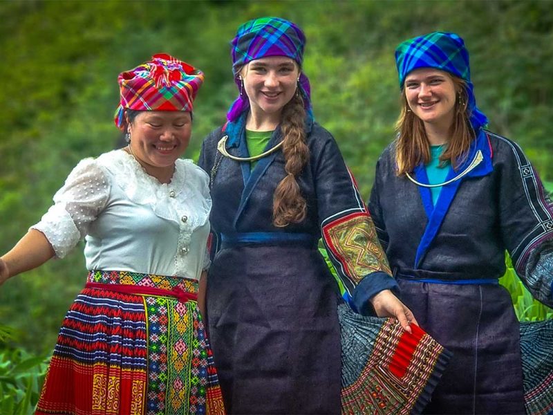 Twee reizigers in geleende traditionele kleding met een lokale vrouw buiten bij een homestay in Mu Cang Chai