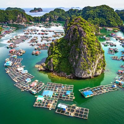 Luchtfoto van een drijvend vissersdorp in Lan Ha Bay, met kleurrijke huisjes, viskwekerijen en kalkstenen eilanden verspreid over het heldergroene water