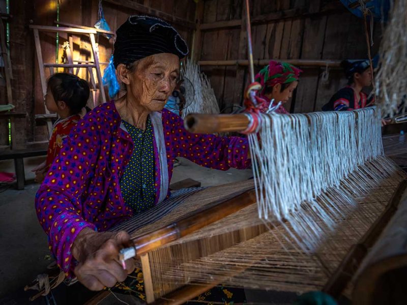 Vrouw uit Lung Tam die traditioneel linnen weeft op een houten weefgetouw