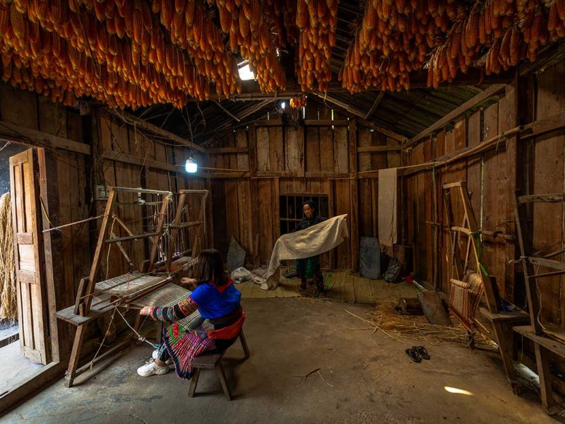 Hmong-vrouwen in Lung Tam Weaving Village in Ha Giang, bezig met traditioneel hennep weven in een houten werkruimte.