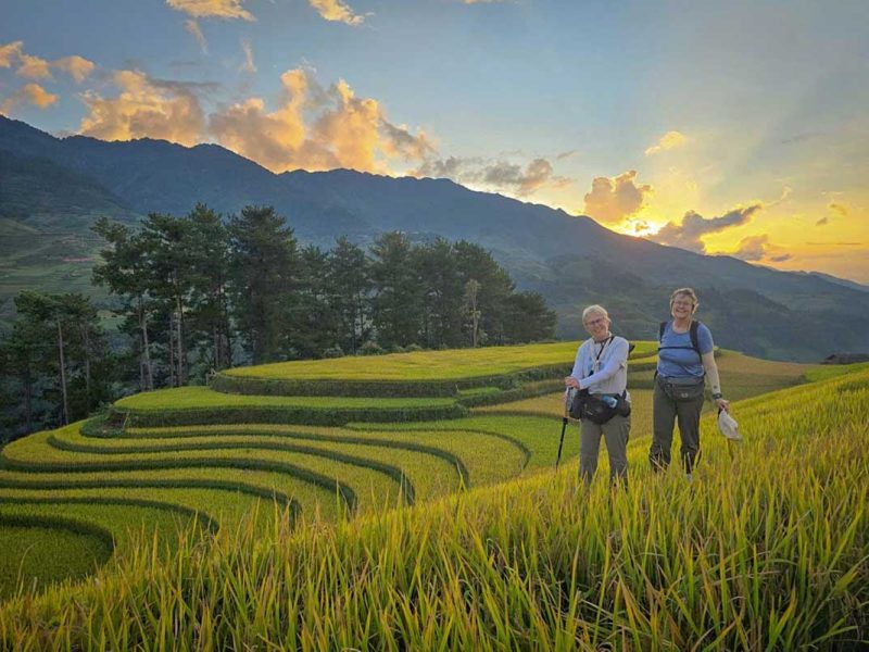 Twee wandelaars in de rijstterrassen van Mu Cang Chai bij zonsondergang achter de bergen