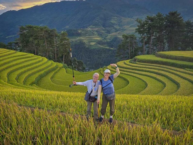 Twee wandelaars poseren tussen de gebogen rijstterrassen van Mu Cang Chai in het late middaglicht