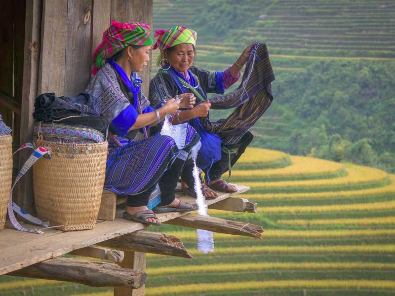 Twee vrouwen naaien op een houten platform met uitzicht over de rijstterrassen van Mu Cang Chai