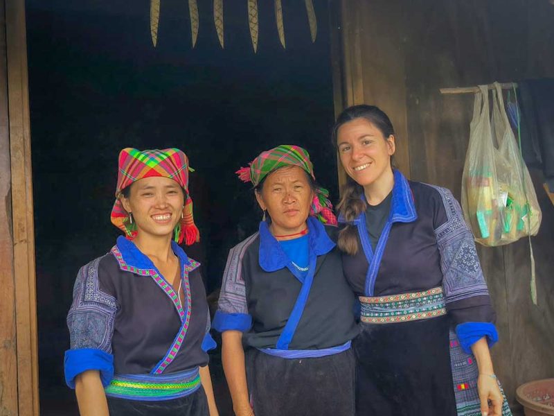 Twee lokale vrouwen en een reiziger in traditionele kleding voor een houten woning in Mu Cang Chai, Yen Bai