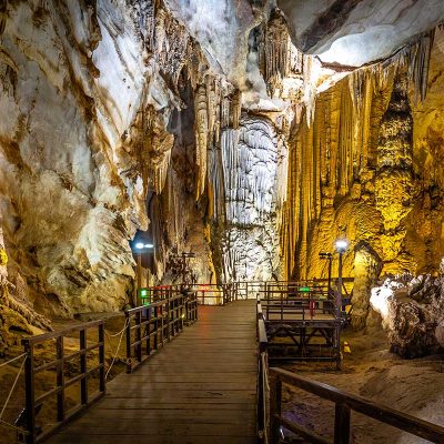 Houten loopbrug in Paradise Cave in Phong Nha, met zicht op hoge grot­wanden en langgerekte stalactieten langs de route.