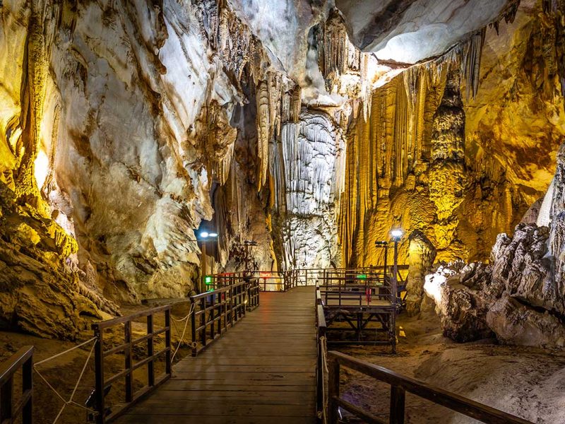 Houten loopbrug in Paradise Cave in Phong Nha, met zicht op hoge grot­wanden en langgerekte stalactieten langs de route.