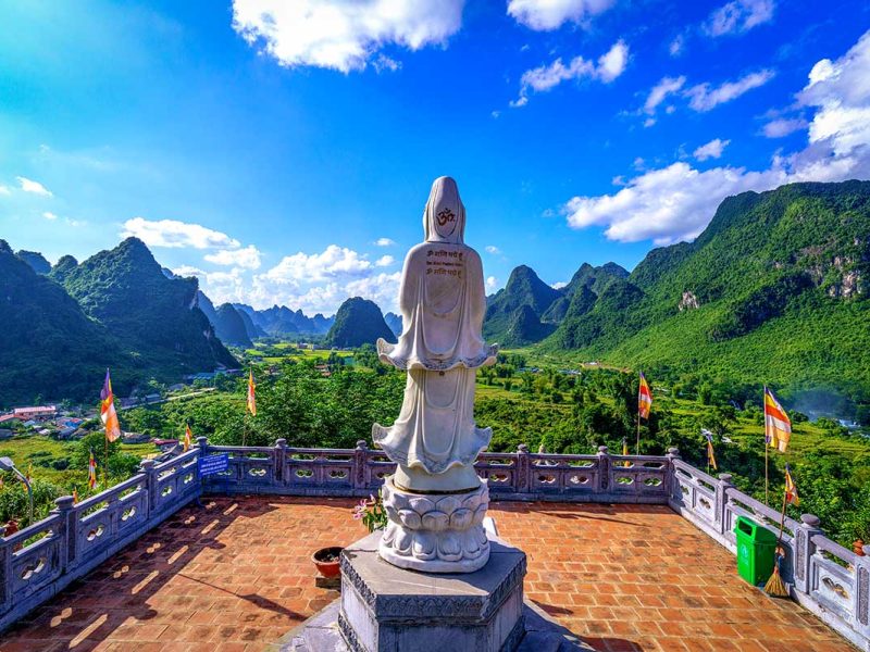 Wit boeddhabeeld op het terras van de Truc Lam pagode met uitzicht over de kalksteenbergen bij Ban Gioc