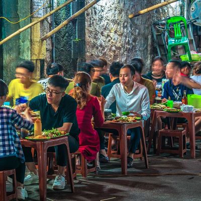 Drukke avond met locals die eten aan kleine tafeltjes op plastic stoeltjes, kenmerkend voor street food in Hanoi en Vietnam