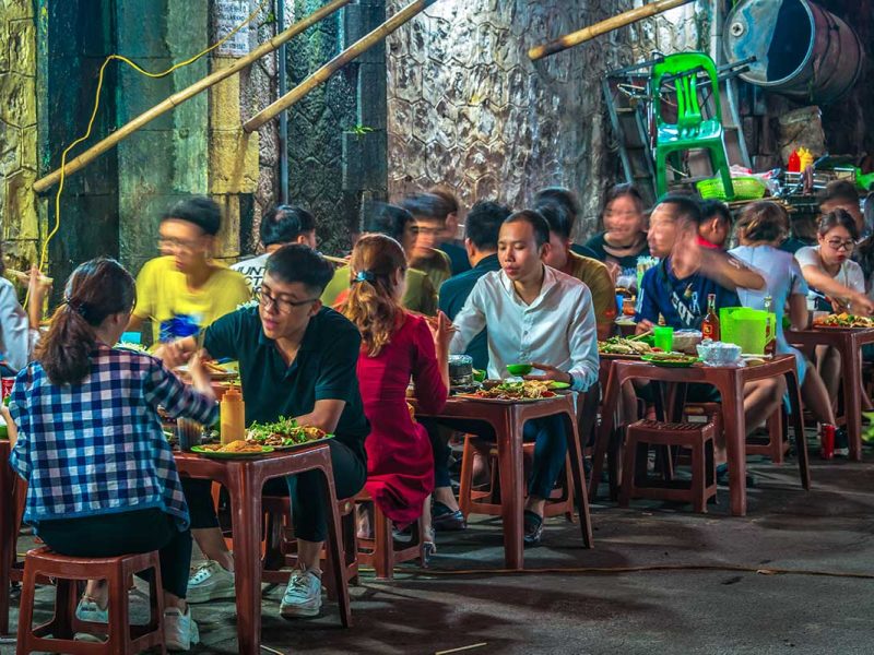 Drukke avond met locals die eten aan kleine tafeltjes op plastic stoeltjes, kenmerkend voor street food in Hanoi en Vietnam