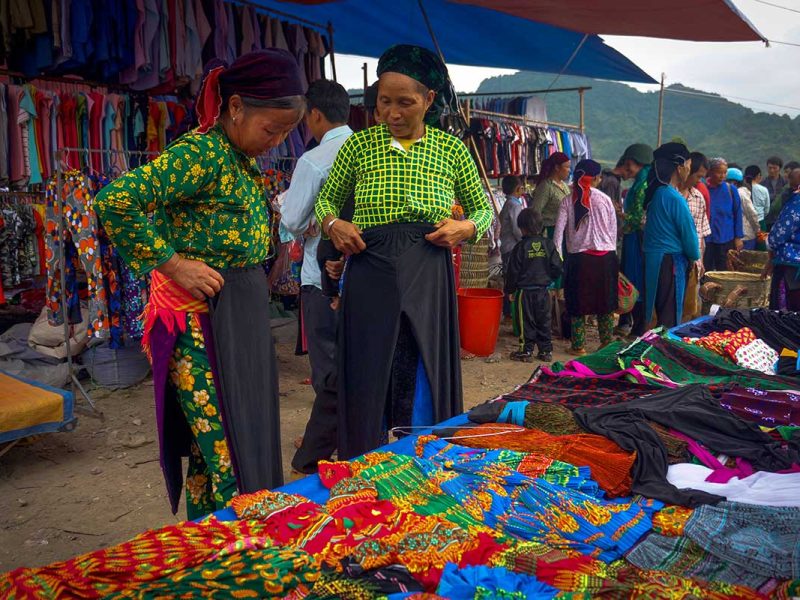 Vrouwen van etnische minderheden op de Quan Ba-markt in Ha Giang, kijkend naar traditionele kleding en kleurrijke stoffen.