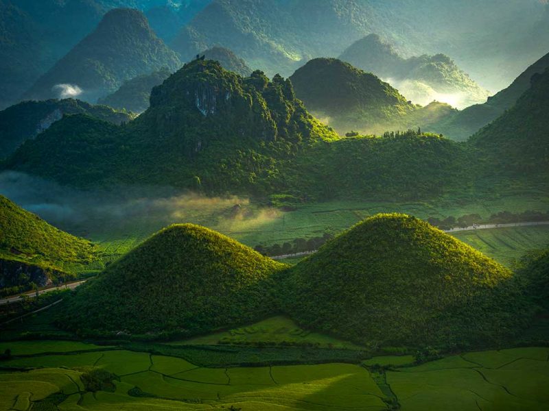 Landschap rond de Quan Ba Twin Mountains met ochtendlicht over groene heuvels.