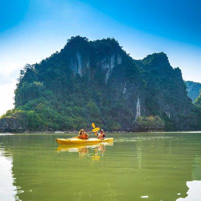 Twee reizigers kajakken door het rustige water van Lan Ha Bay, omringd door steile kalkstenen eilanden en groene kliffen tijdens een cruise bij Cat Ba Island