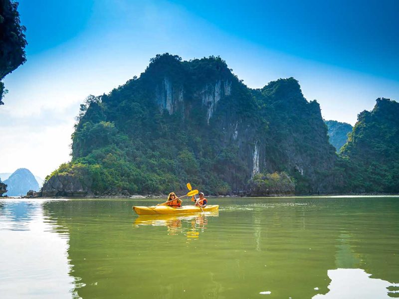 Twee reizigers kajakken door het rustige water van Lan Ha Bay, omringd door steile kalkstenen eilanden en groene kliffen tijdens een cruise bij Cat Ba Island
