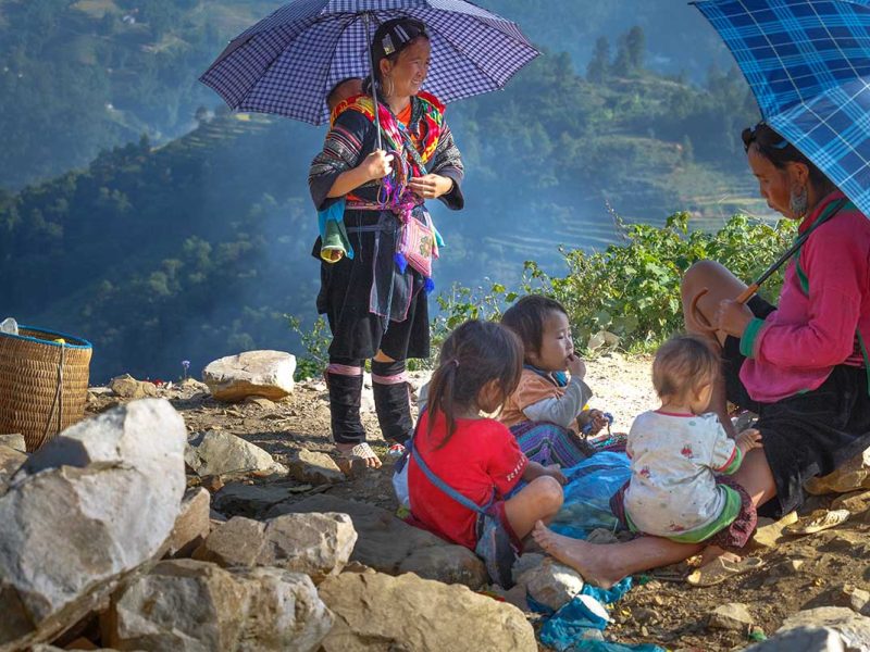 Etnische vrouwen en kinderen uit de regio Sapa rusten langs een bergpad, een intiem moment voor documentaire en portretfotografie in Noord-Vietnam.