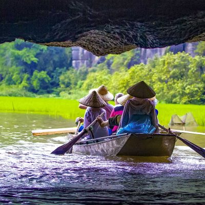 Roeiboot vaart door een grot tijdens een Tam Coc boottocht in Ninh Binh, met rijstvelden, kalksteenrotsen en lokale roeiers