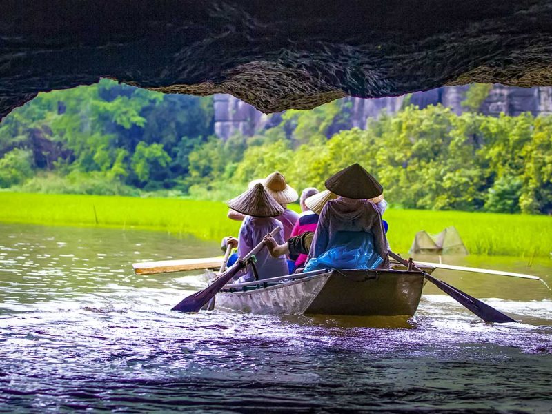 Roeiboot vaart door een grot tijdens een Tam Coc boottocht in Ninh Binh, met rijstvelden, kalksteenrotsen en lokale roeiers